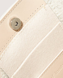 Close-up of the beige leather Jaunt Midi Tote by Graf Lantz, showcasing a magnetic button clasp. Its visible stitching and textured detail perfectly complement the light suede flap. Inside, discover card slots and a subtly embossed brand name on this elegant mid-size carryall.