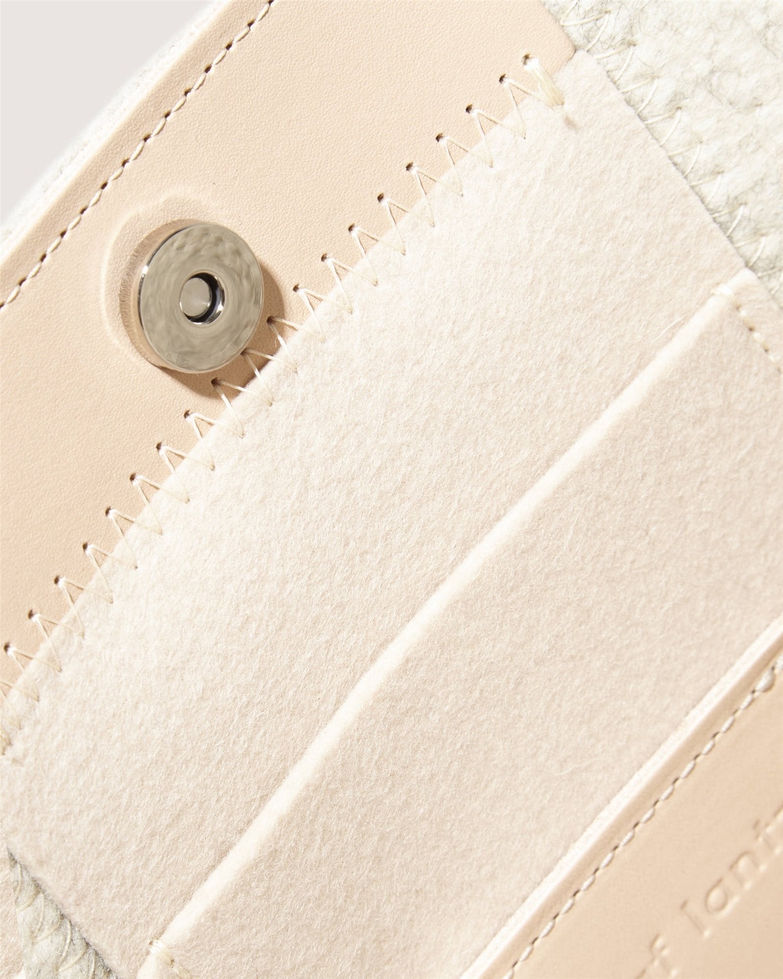 Close-up of the beige leather Jaunt Midi Tote by Graf Lantz, showcasing a magnetic button clasp. Its visible stitching and textured detail perfectly complement the light suede flap. Inside, discover card slots and a subtly embossed brand name on this elegant mid-size carryall.