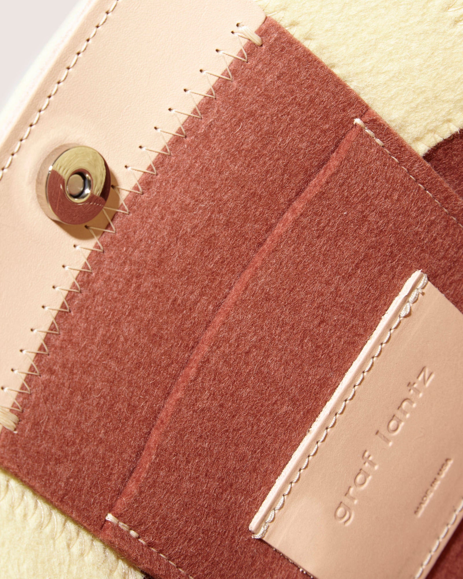Close-up of the Graf Lantz Jaunt Midi Tote shows a magnetic snap closure, crafted from beige and brown Merino wool felt and leather with visible stitching. A text-printed leather label completes this stylish mid-size carryall.
