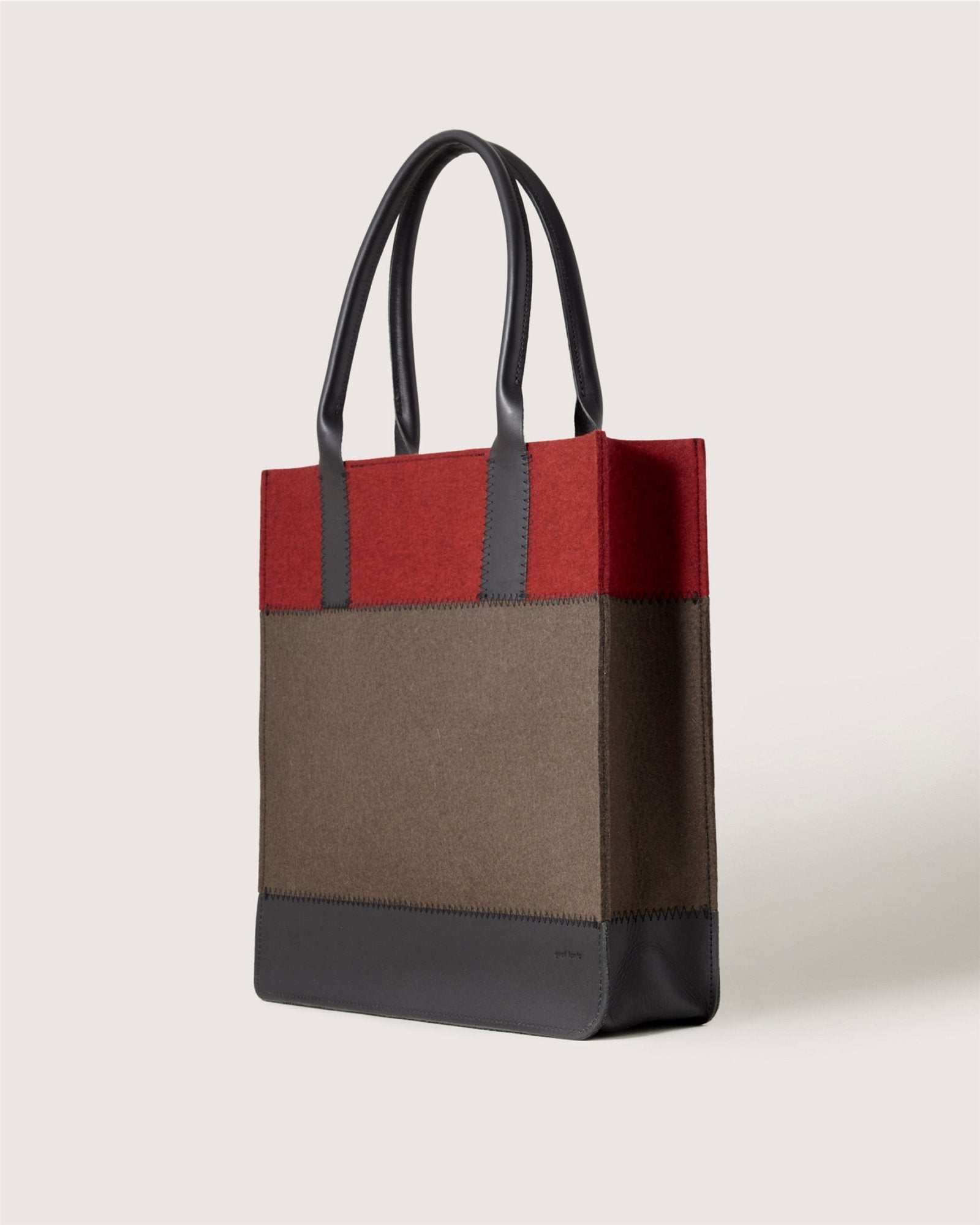 The Graf Lantz tote bag features two black handles and a color-block design with a red top, brown middle, and black base, displayed on a plain light background.