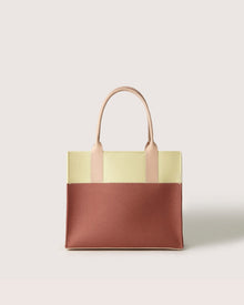 The Graf Lantz Jaunt Midi Tote is a chic, mid-size carryall with a color-block design, featuring a yellow upper, brown lower section, and beige leather handles. The structured rectangular shape stands out against a plain white background.