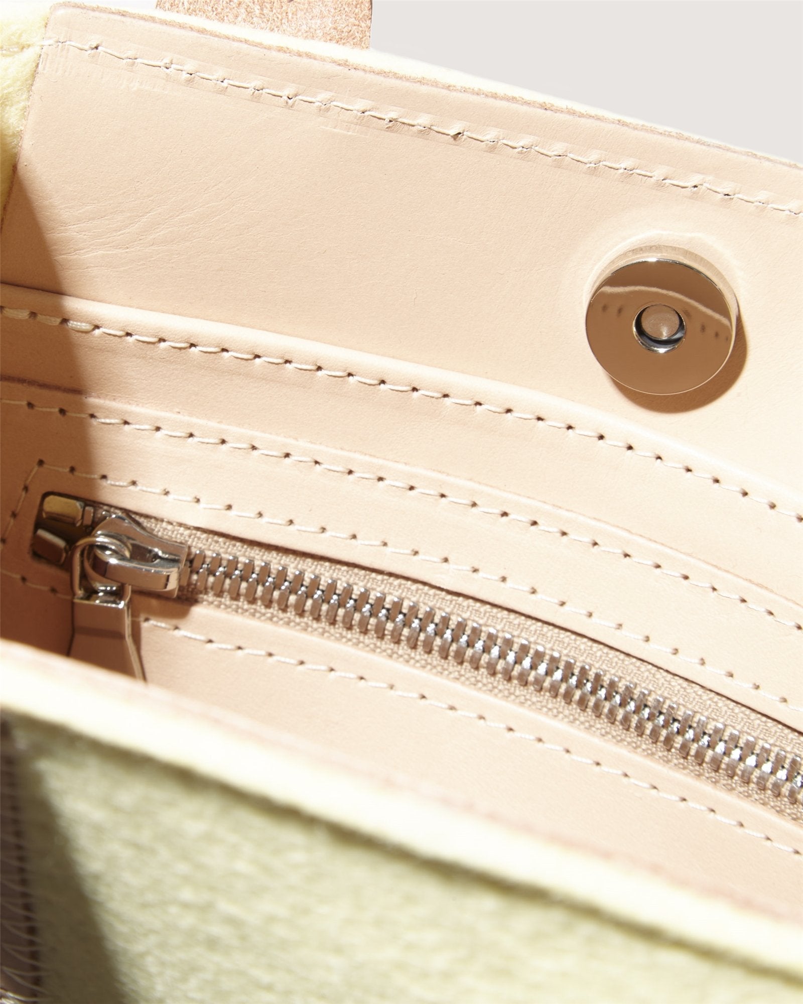 A close-up of Graf Lantzs beige leather mini tote showcases its versatile interior, featuring a zippered pocket and button closure. The soft, textured fabric is elegantly detailed with neat stitching, making it suitable for any occasion.