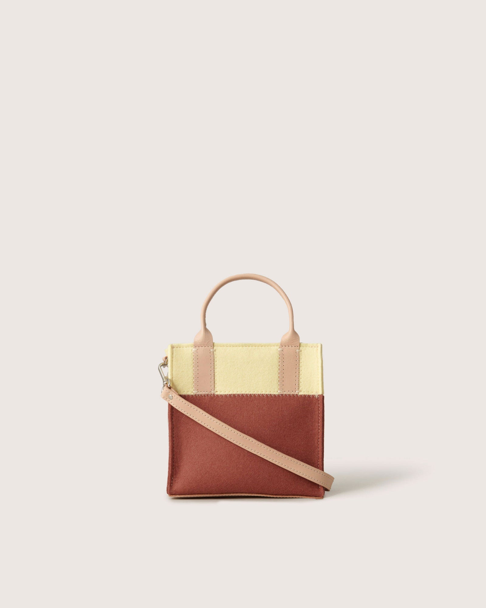 The Graf Lantz mini tote offers a top handle and shoulder strap, showcasing a color block design with yellow and brown panels, complemented by a beige handle and strap on a plain light backdrop.