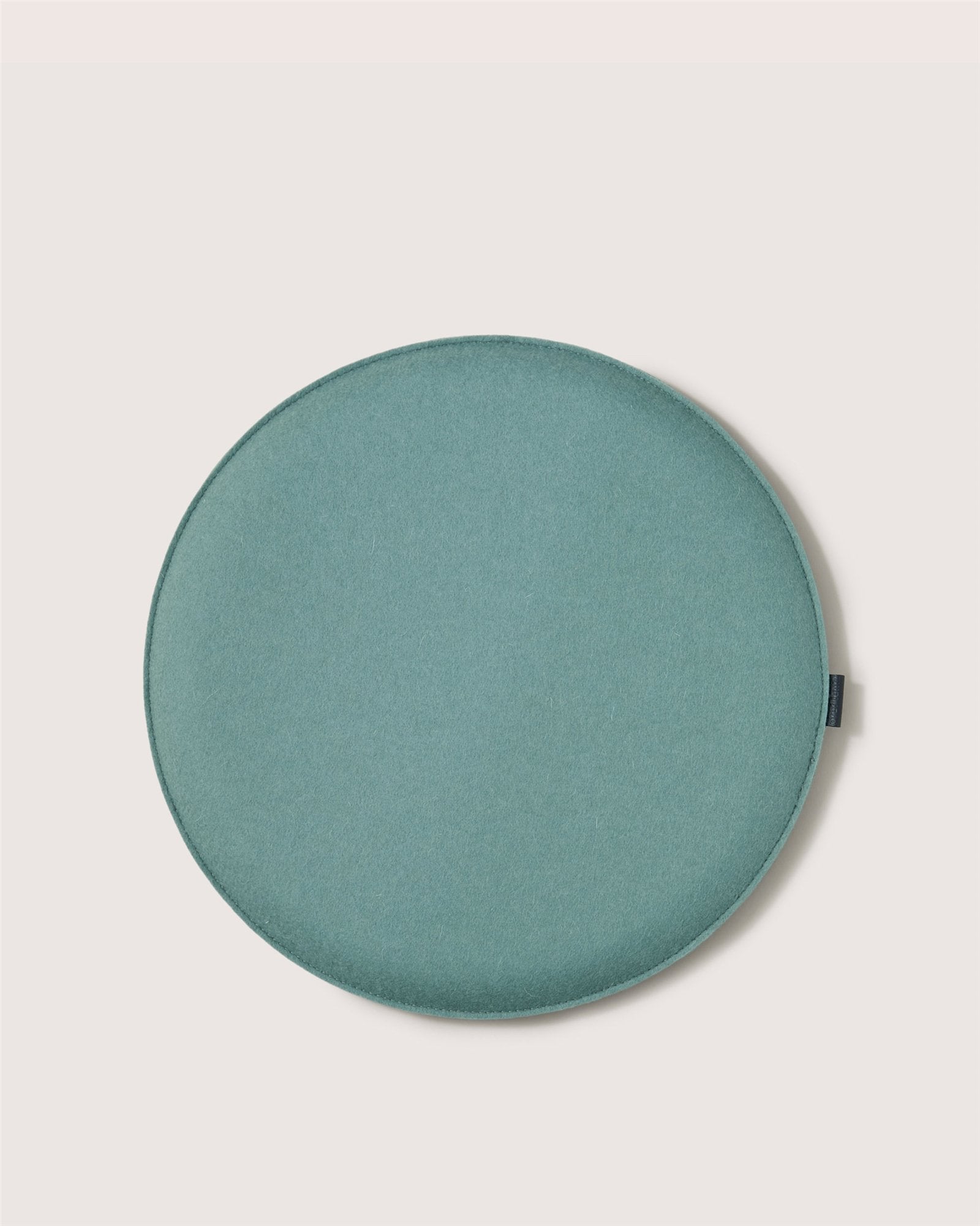A round, flat, teal fabric cushion by Graf Lantz, this stylish seat is ideal as a meditation or Zabuton Seat Cushion, displayed on an off-white background.