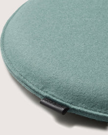 A close-up of a round, teal Graf Lantz felt meditation cushion shows soft texture, visible edge stitching, and a small black fabric tag. The light neutral background perfectly highlights this elegant Graf Lantz Zabuton Seat Cushion.
