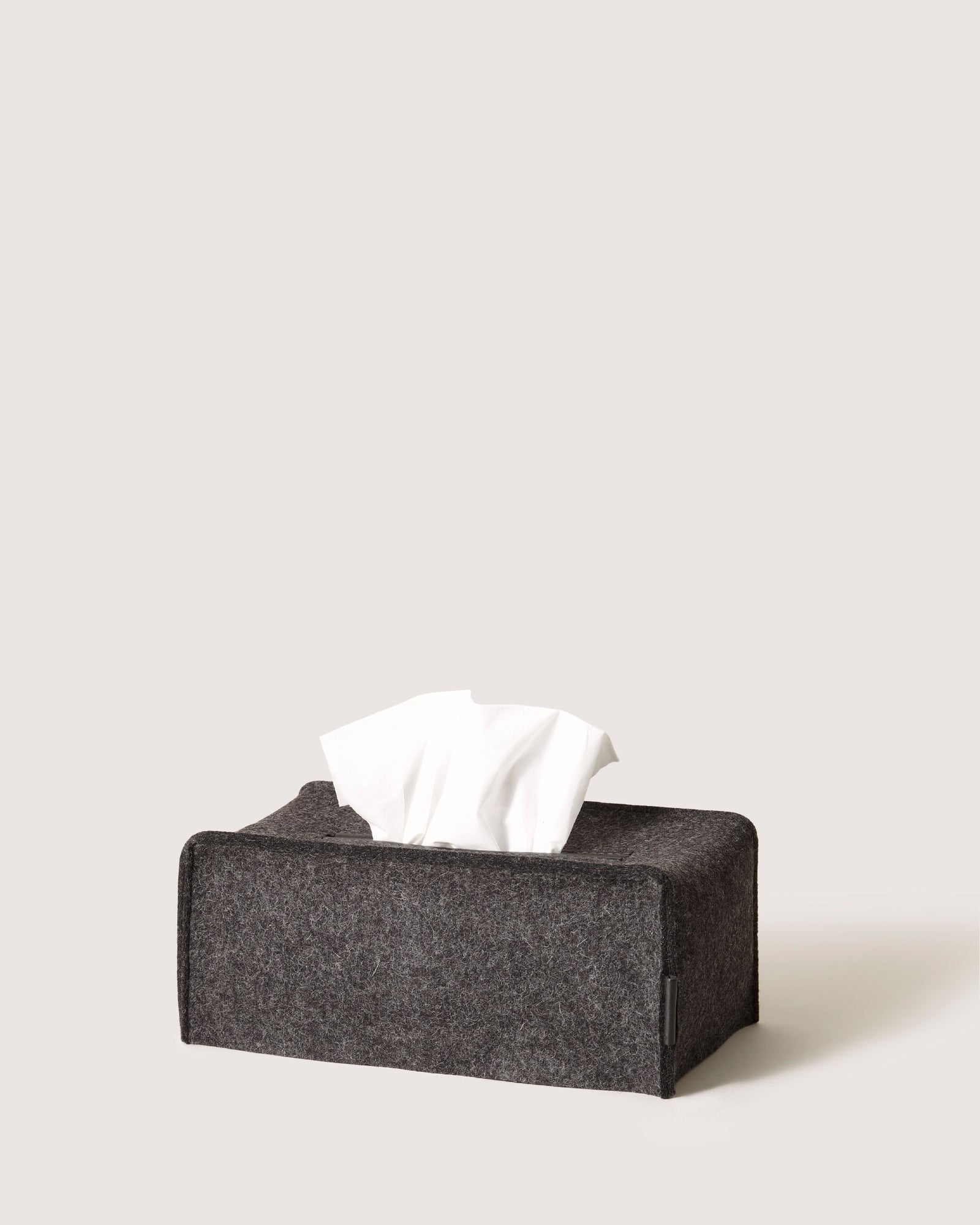The graf lantz dark gray, rectangular tissue box with a fabric texture captures a minimalist silhouette. White tissues are partially pulled out, and it sits elegantly against a plain, light background, exuding an understated charm.