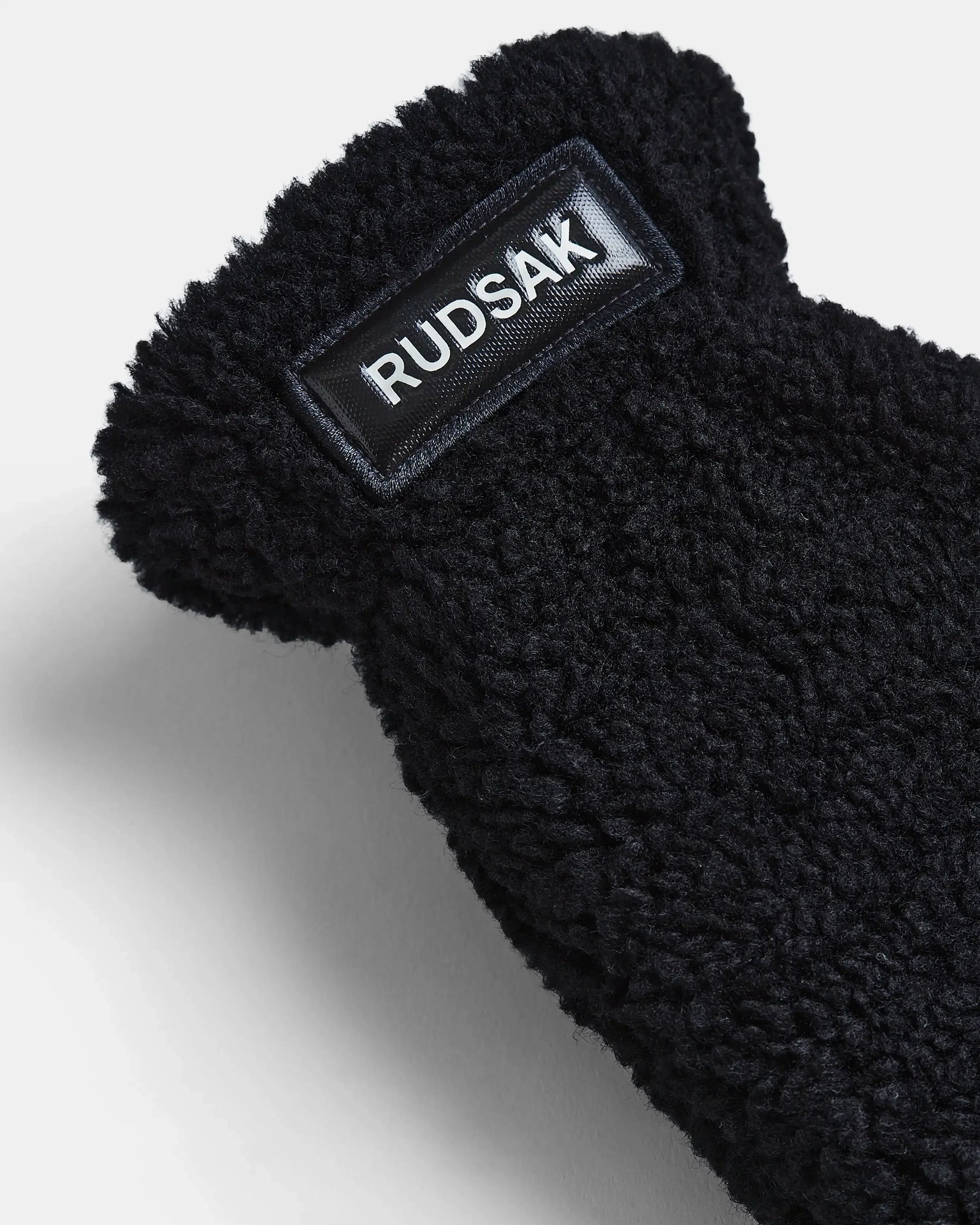 Close-up of SUSAN S - 8423511 Black by Rudsak, showing black textured fleece-like fabric with a rectangular brand patch—ideal for women’s teddy faux fur mittens.
