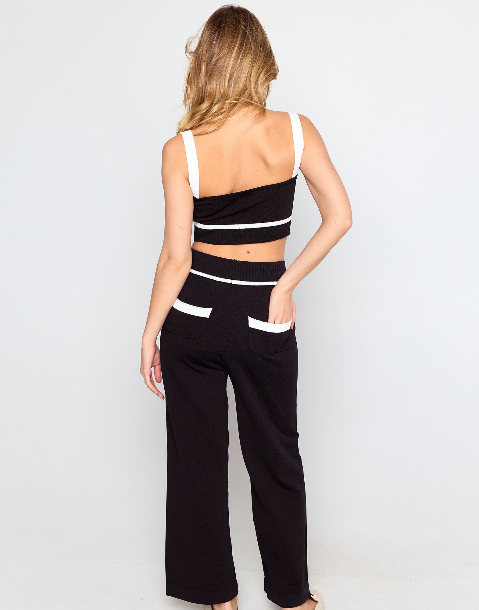 Woman wearing a black and white outfit with wide-leg pants on a plain background