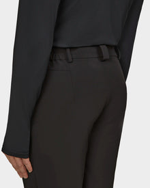 A person wearing Rudsak KICO - 6523508 Black tailored pants and a black long-sleeve top, seen from the back and waist down with one arm resting by their side.