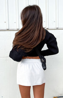 Back view of a white mini skirt featuring a ruched elastic waistband and a subtle textured fabric