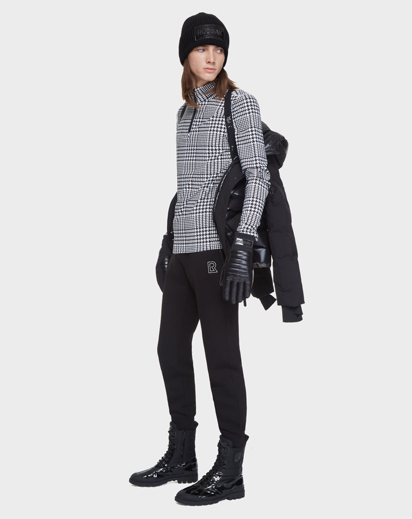 A person dressed in black holds the Rudsak DUSK - M121506 BLACK men’s puffer jacket with waterproof zippers over one shoulder against a plain white background.