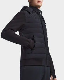 A person wears the Rudsak LAURENZO - M123514 Black quilted zip-up puffer vest with removable hood over a black long-sleeve top and dark pants, standing against a plain white background.