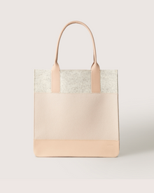 The Graf Lantz Jaunt Midi Tote is a chic, mid-size carryall in light beige and cream blocks. It features two sturdy handles and is crafted from luxurious Merino wool, offering a simple, modern design that stands out beautifully against a plain background.