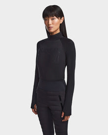 A woman with straight long black hair wears Rudsak's KILTON - 8523533 Black fleece-lined jersey top and black pants, standing against a plain white background—an effortlessly chic look for any winter wardrobe.