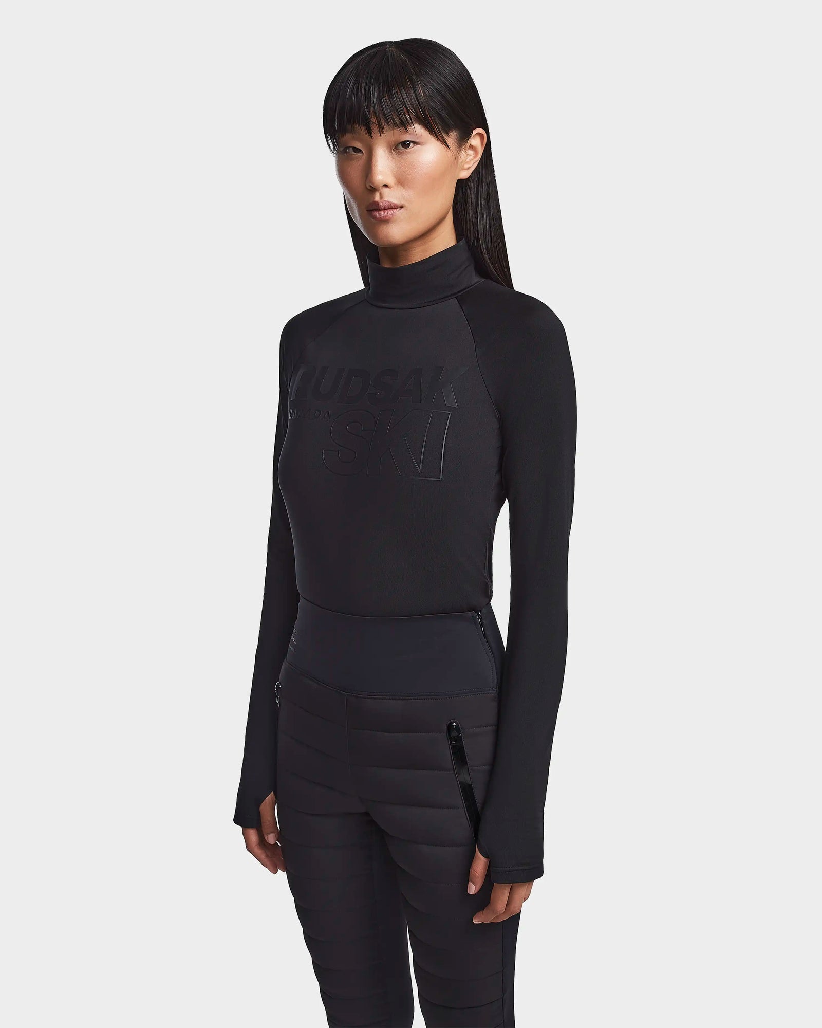 A woman with straight long black hair wears Rudsak's KILTON - 8523533 Black fleece-lined jersey top and black pants, standing against a plain white background—an effortlessly chic look for any winter wardrobe.