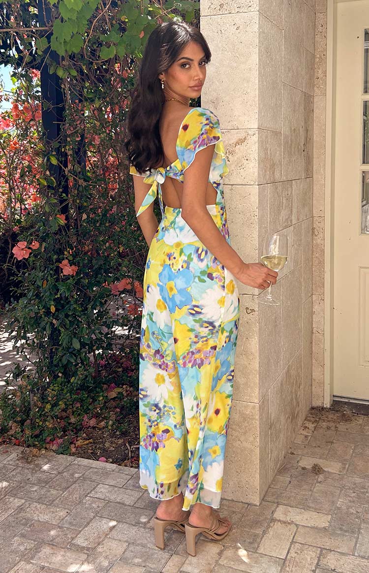 Rear view of a blue and yellow floral chiffon maxi dress with an open back and tie-up bow detail