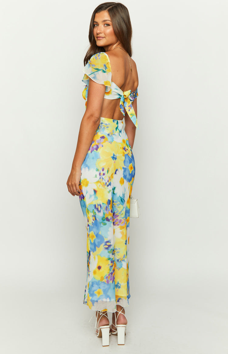 Rear-side view of a blue and yellow floral chiffon maxi dress with a tie-back detail and waist cutouts