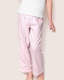 A child is wearing Petite Plumes Kids Twill Pajama Pants in Pink Gingham, crafted from yarn-dyed cotton, paired with a white top. The photo shows the lower body against a plain backdrop, emphasizing the slightly loose and comfy fit of the sleepwear.
