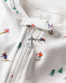 Close-up of Petite Plumes Babys Pima Romper in Apres Ski, showcasing a cozy fabric with a zipper adorned with small skier illustrations and scattered green trees, ideal for sleepwear.