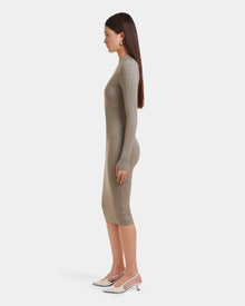 A woman in profile wears the MAYLIN - 8523504 Cement Pattern dress by Rudsak, a womens fitted midi crafted from stretch fabric. She pairs the beige dress with white slingback heels; her straight brown hair stands out against a plain white backdrop.