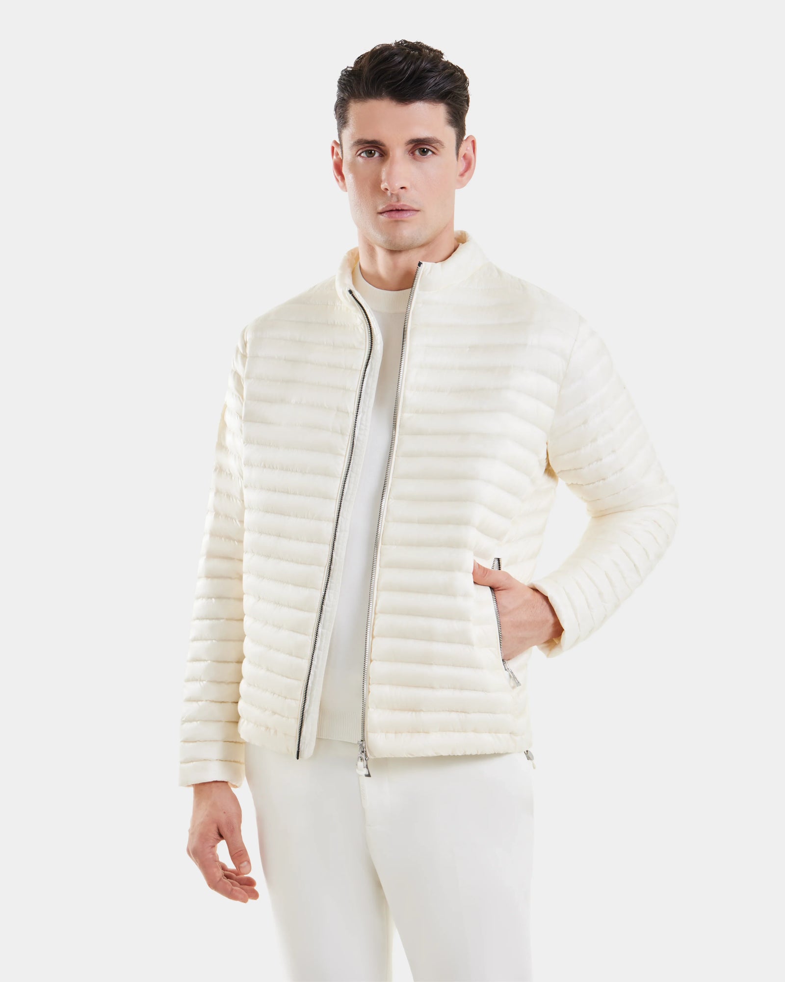 A man wears the Rudsak REYMOND - M125013 Iceland white quilted men’s down jacket with RDS-certified down over white shirt and pants, standing against a plain white background with his left hand in his pocket.