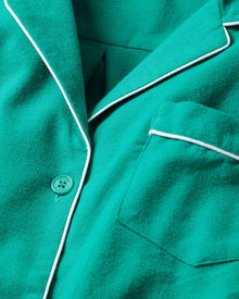 Close-up of Petite Plumes Kids Flannel Pajama Set in Forest Green, featuring white piping, button, and pocket. The soft material and bright color in a simple design make it eye-catching sleepwear for children.