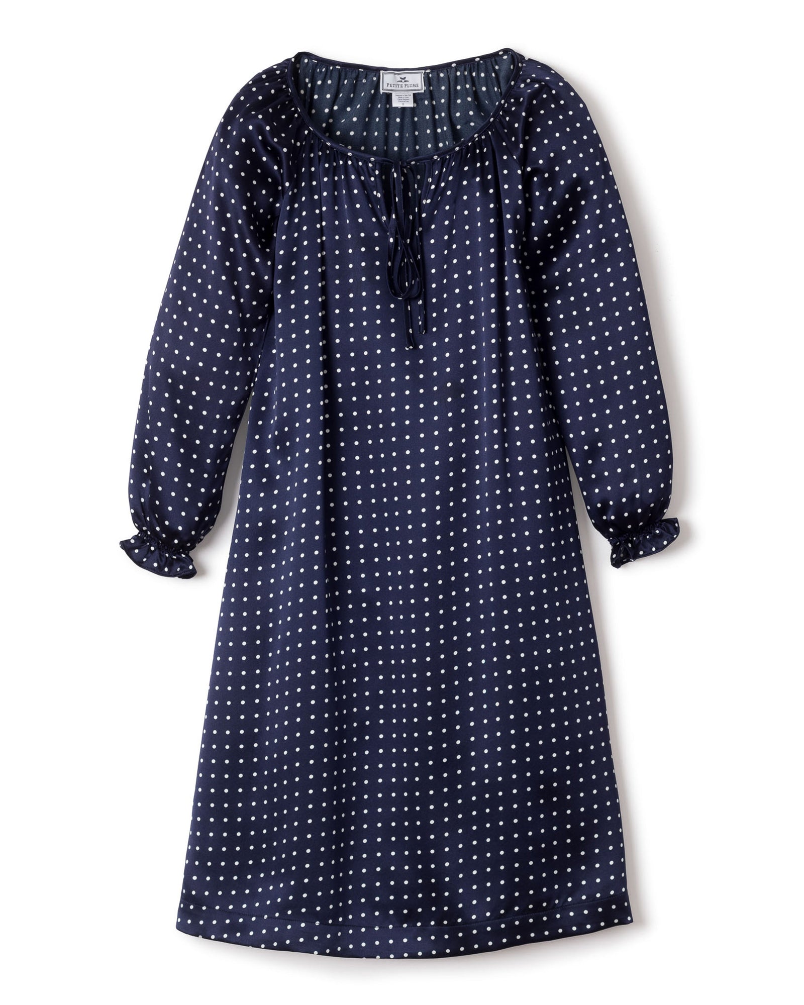 The Girls Silk Delphine Nightgown by Petite Plume is a navy blue sleepwear adorned with white polka dots, featuring long sleeves, a ruffled neckline with a tie, and slightly gathered cuffs.