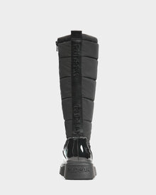 A black, knee-high women's quilted winter boot by Rudsak, CLAUDE - L223506, shown from the back with glossy heel and sole accents, featuring RUDSAK branding vertically on the back strap and heel.