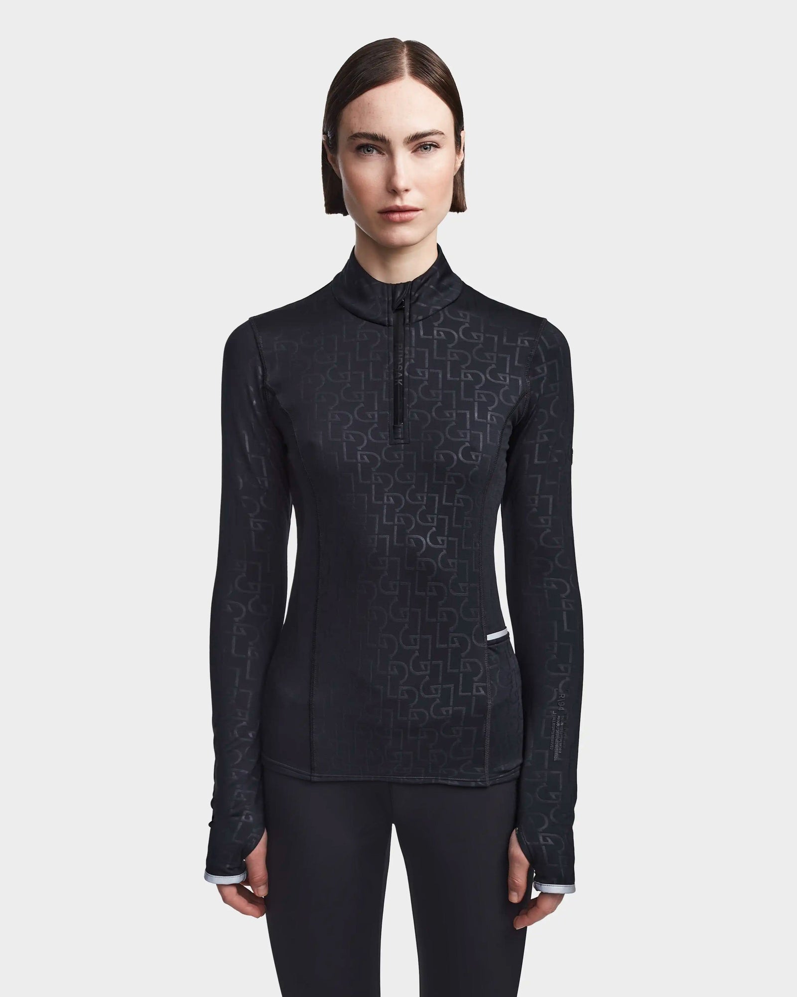 A woman with straight brown hair models the Rudsak SIRE - 8523531 Black Pattern fitted, fleece-lined jersey ski top with a subtle geometric print and short front zipper against a plain light gray background—ideal for cold weather.