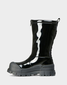 The KRISTAL HI - 8222510 BLACK by Rudsak is a black, mid-calf high-gloss winter boot with chunky grip soles, a thick gray rubber toe cap, side zipper, and back lacing detail, shown on a plain light background.