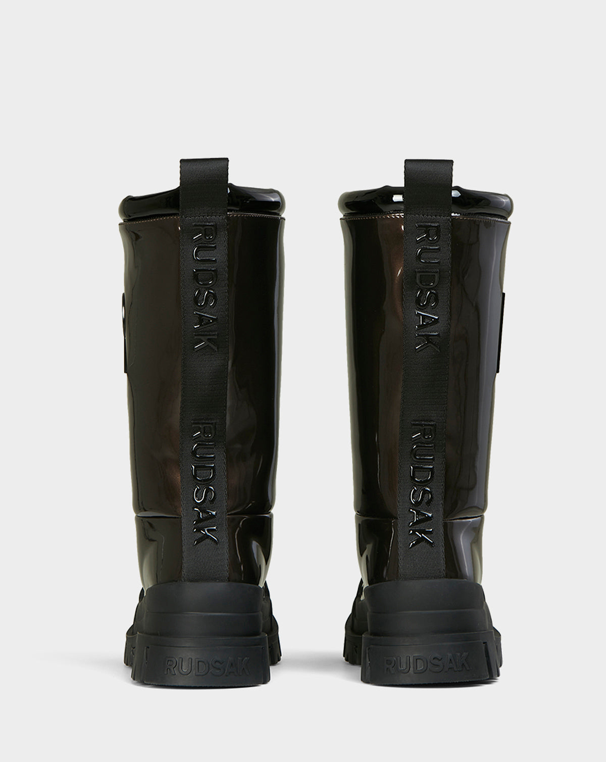 Two KRISTAL HI - METALLIC CHOCOLATE boots by Rudsak are shown from the back. These womens boots have chunky grip soles and black pull tabs with Rudsak printed vertically in bold. The background is plain white.