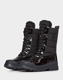 The Rudsak LEX - 8222501 BLACK women’s winter boots feature black patent panels, thick rubber soles, insulated padded uppers, metal eyelets, faux fur trim, and a side emblem—perfect for staying warm and stylish.