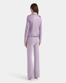 A woman with straight brown hair stands facing away, wearing the Rudsak MERGO - 8124034 Lilac Foam biker jacket and matching wide-legged pants with high heels against a plain white background.