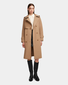 A woman wears the Rudsak KINDA - 8124690 Camel trench coat over a white collared shirt, black skirt, and knee-high black boots against a plain light background.