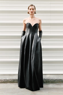 Woman wearing a black leather strapless bustier gown with a full skirt and black gloves.