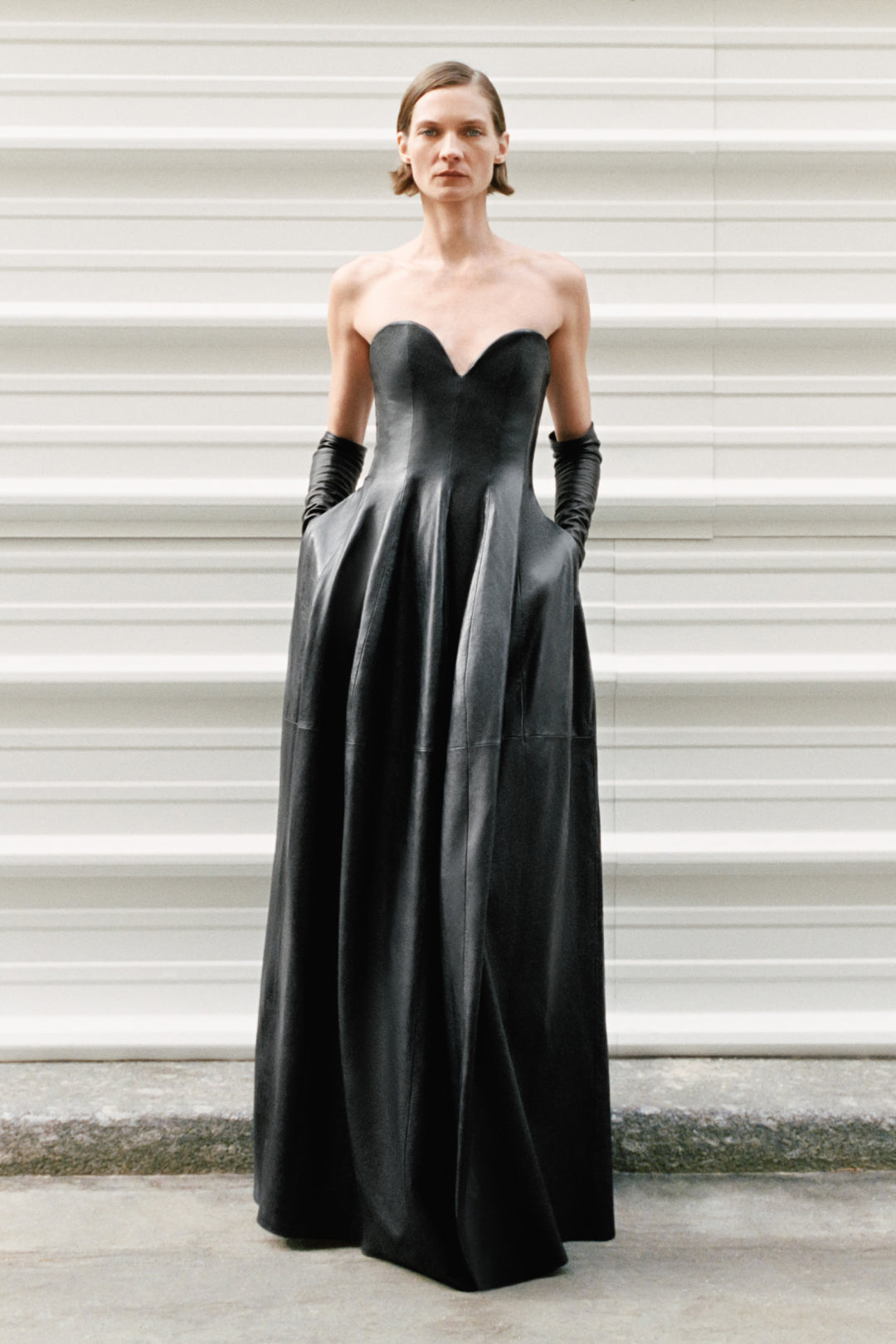 Woman wearing a black leather strapless bustier gown with a full skirt and black gloves.