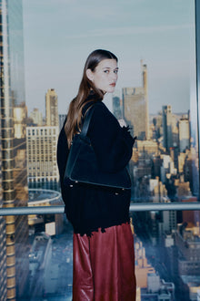 Black wool sweater with ribbed texture and oversized fit, worn over red skirt.