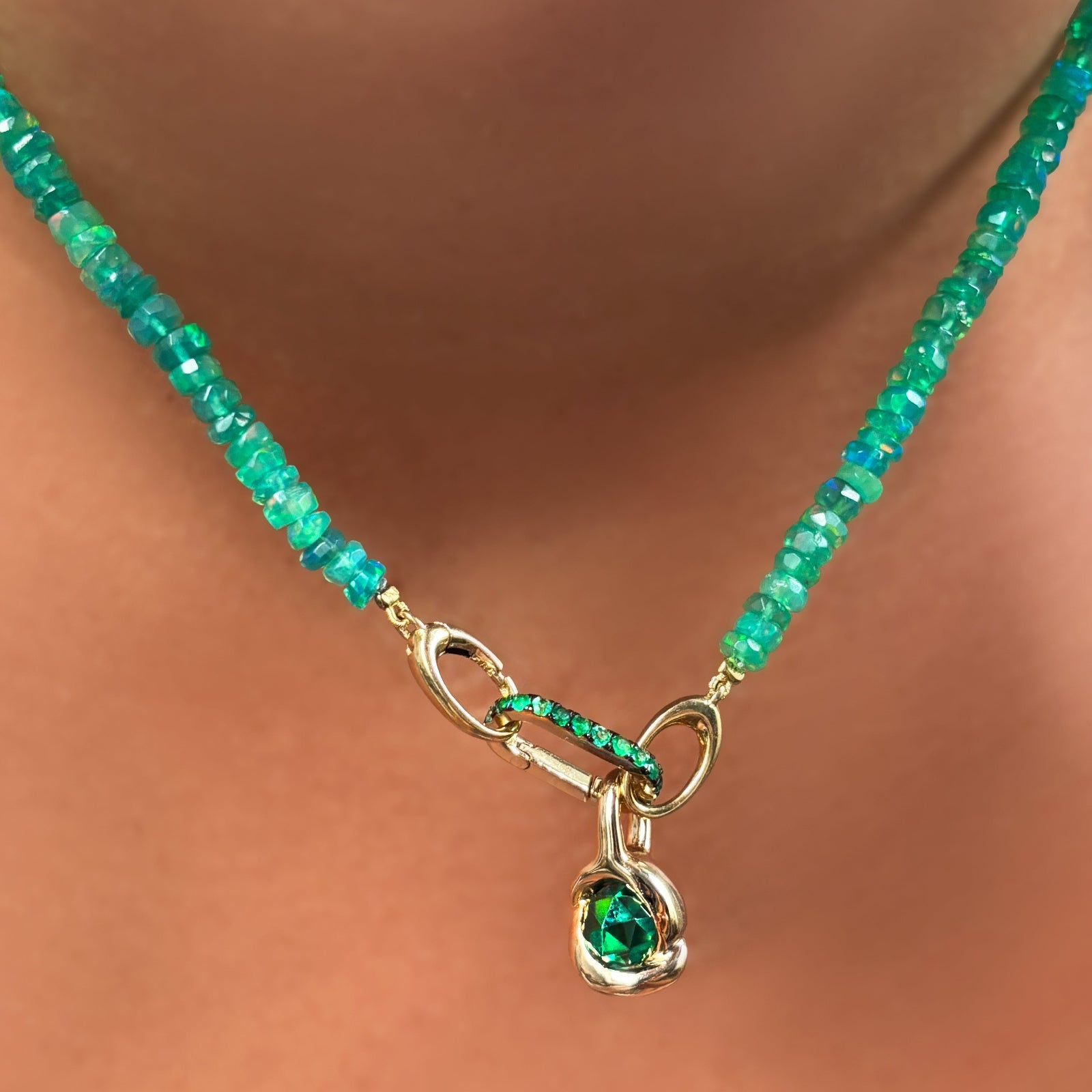Green faceted opal necklace with emerald knot charm and small emerald charm lock on a person's neck.
