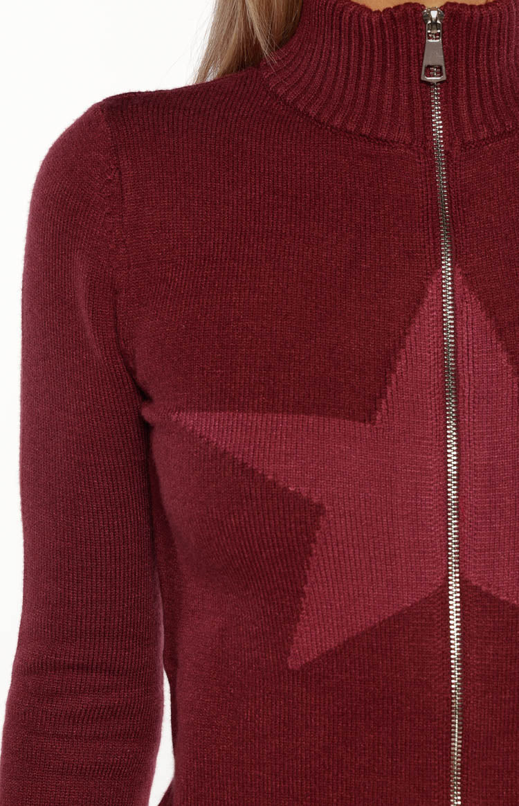 Close-up of the burgundy knit sweater showing the ribbed mock neck, silver zip, and darker star pattern