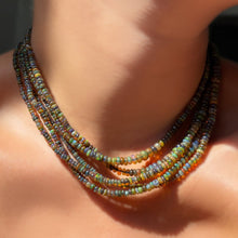 A neck full of labradorite grey opal necklaces on the skin, in sunlight.