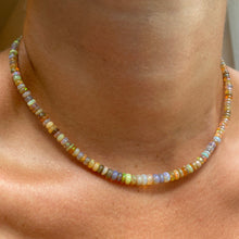 Shimmering beaded necklace made of smooth opal rondels in shades of light yellow, light orange, white, and brown on a slim gold lobster clasp, styled on a neck