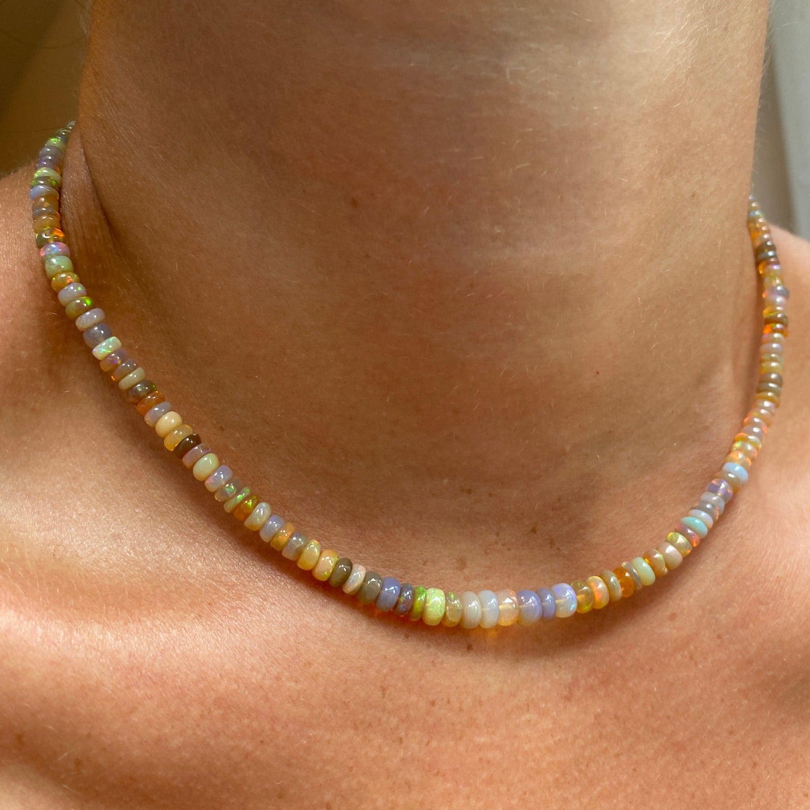 Shimmering beaded necklace made of smooth opal rondels in shades of light yellow, light orange, white, and brown on a slim gold lobster clasp, styled on a neck