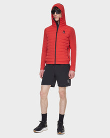 A person stands against a white background wearing RUDSAK’s JARRY - 6122007 POPPY RED water-resistant jacket, black shorts, black socks, black sneakers, and sunglasses.
