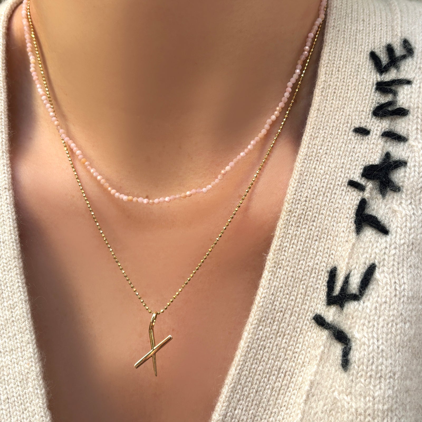 Slim gemstone necklace in pink opal with diamond cut bead chain with letter "x" charm on a model's neck.