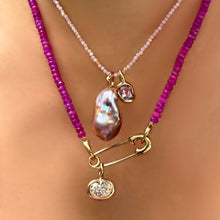 slim gemstone necklace in pink opal with an amethyst knot charm + blush baroque pearl charm, layered with a safety pin charm lock on a fuchsia faceted opal necklace with an oval diamond solitaire charm hanging from it.