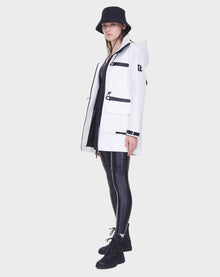 A person wearing the Rudsak CAMY - 8122002 WHITE mid-length raincoat stands against a plain white background, styled with a black bucket hat, shiny black leggings, and black lace-up boots.